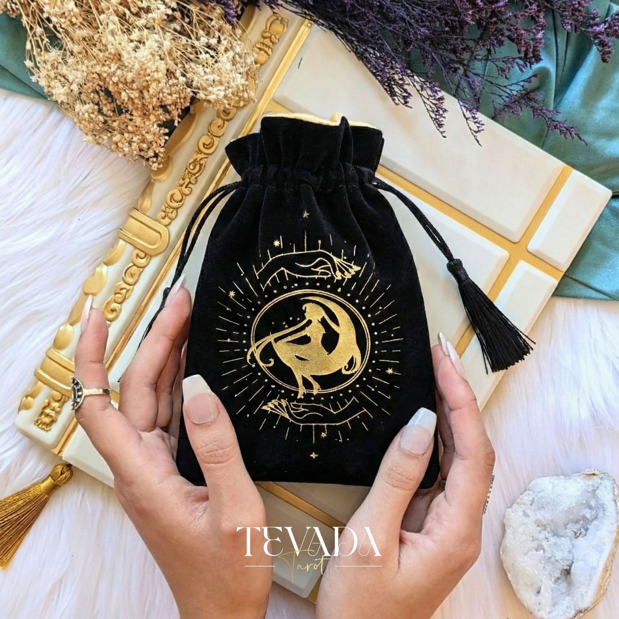 Bolsa de tarot de terciopelo negro con estampado dorado y borlas para proteger barajas de tarot y cristales en un altar de brujas.