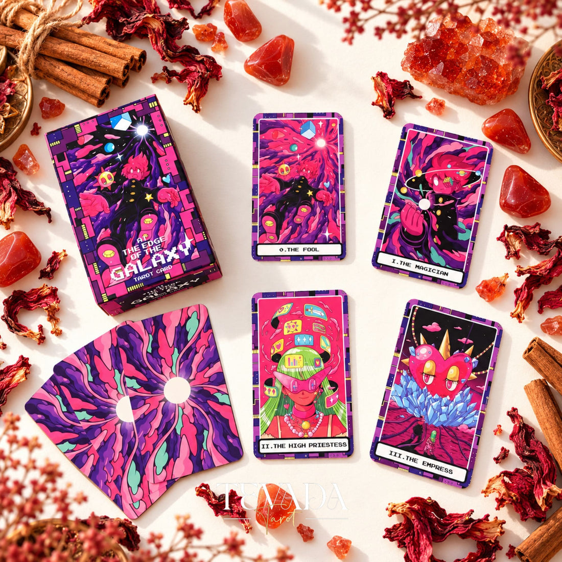 At the Edge of the Galaxy Tarot box with neon illustrated card fronts and a purple sunburst card back, surrounded by red flowers and crystals.