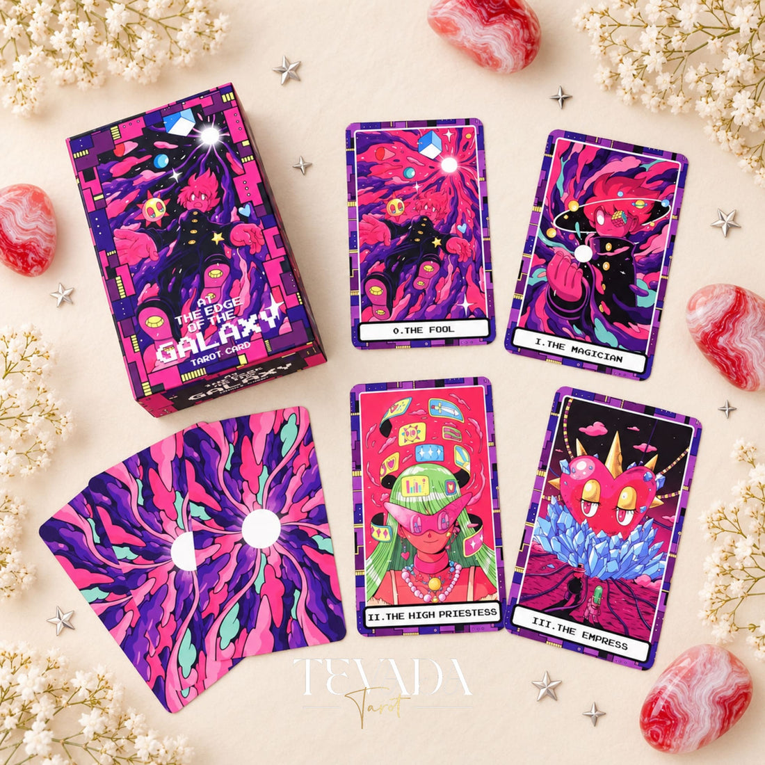 At the Edge of the Galaxy Tarot box with colorful card fronts and purple sunburst card backs, arranged among white flowers and pink stones.