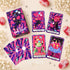 At the Edge of the Galaxy Tarot box with colorful card fronts and purple sunburst card backs, arranged among white flowers and pink stones.