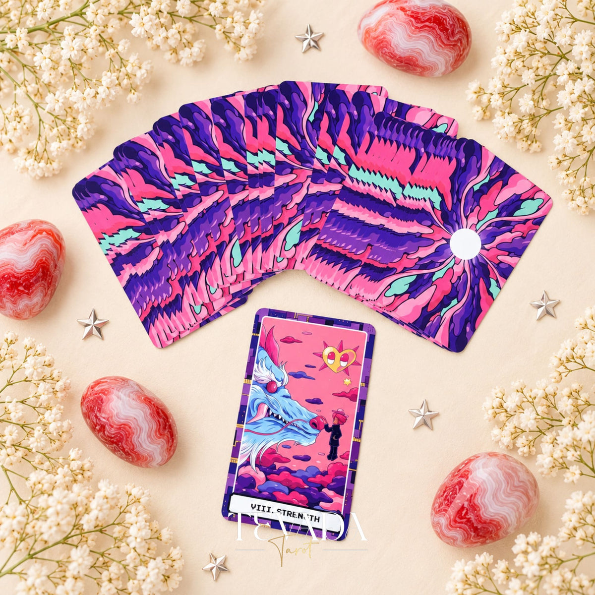 At the Edge of the Galaxy Tarot purple sunburst card backs fanned above The Fool card, surrounded by white flowers and pink stones.