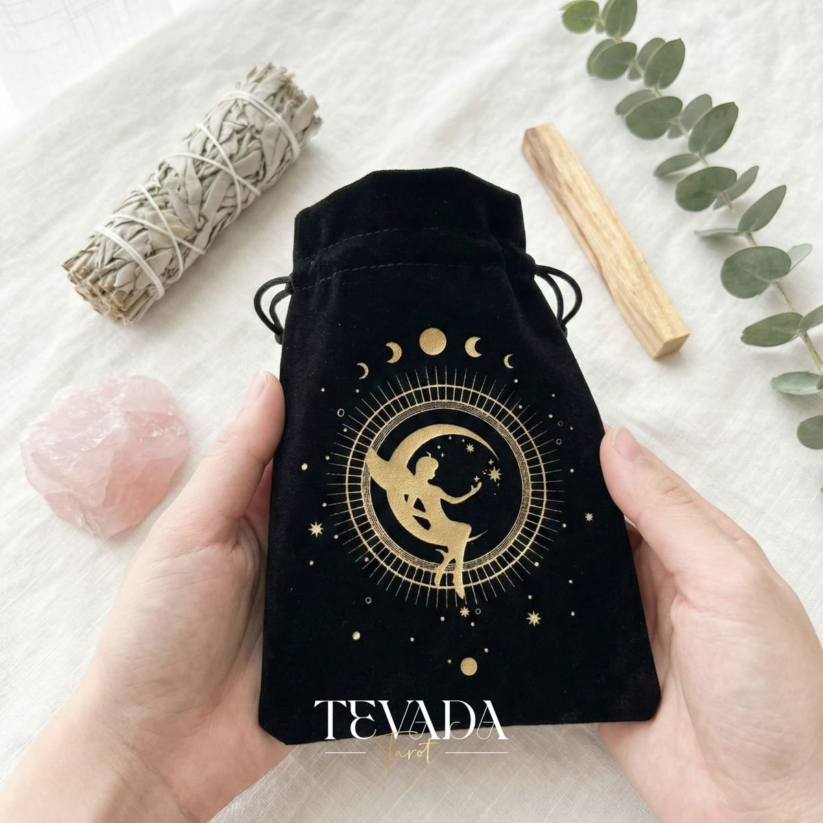 Bolsa de tarot de terciopelo negro con estampado dorado y borlas para proteger barajas de tarot y cristales en un altar de brujas.