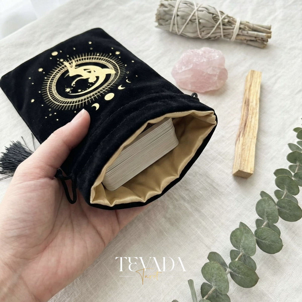 Bolsa de tarot de terciopelo negro con estampado dorado y borlas para proteger barajas de tarot y cristales en un altar de brujas.