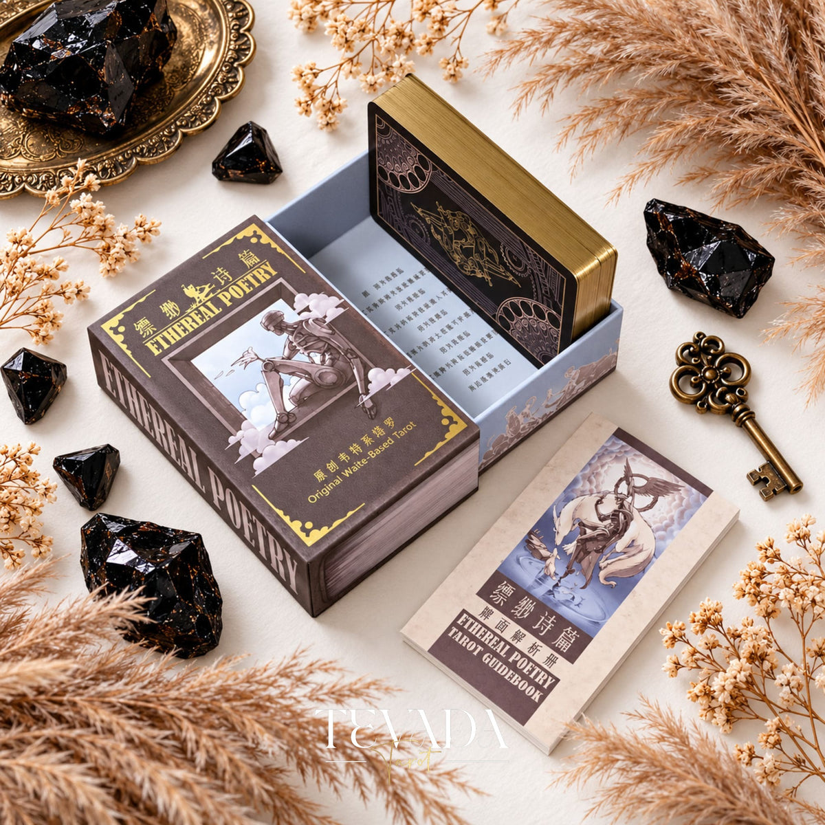 Ethereal Poetry Tarot Deluxe open rigid box with an illustrated lid, guidebook and tarot card, surrounded by black crystals and dried grasses.