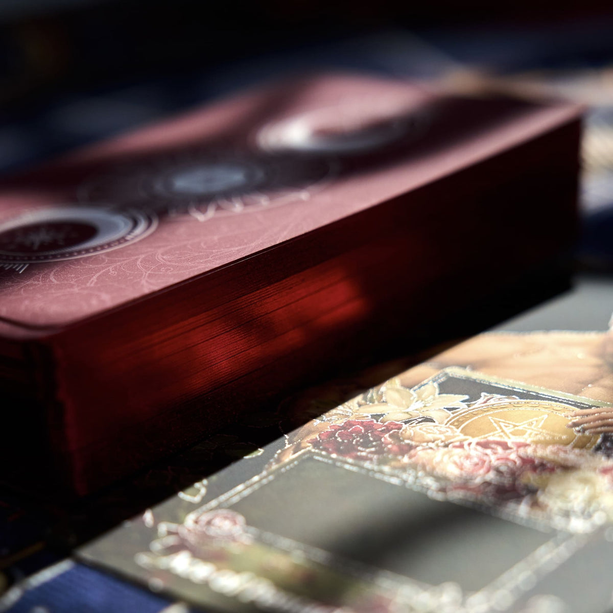 Pact of the Arcana Tarot deck and cards arranged beside the maroon patterned box with silver foil accents