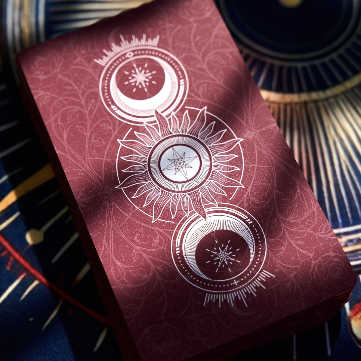 Close-up of the maroon Pact of the Arcana Tarot card back with celestial sun and star emblems