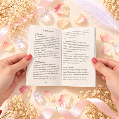 The Covenant Tarot open English guidebook held in two hands on a pink floral background.