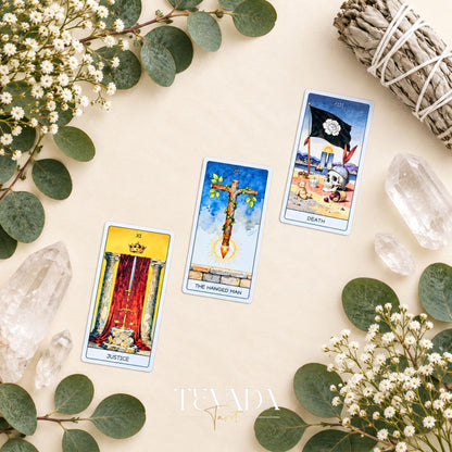 The Justice, Hanged Man and Death tarot cards arranged on a pale leafy background with white flowers and crystals.